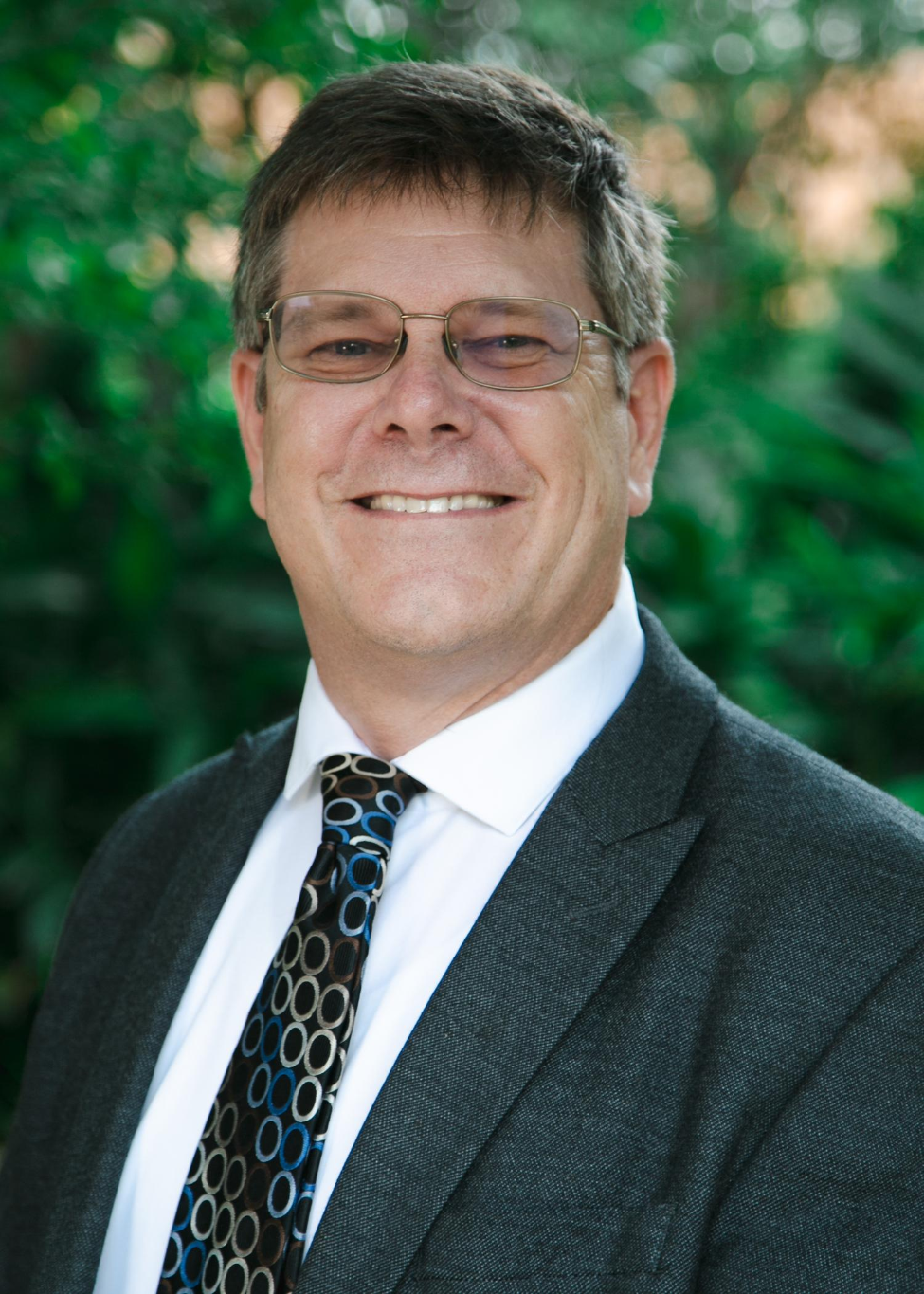 William “Brett” Perkison, MD, MPH, in front of greenery for a headshot.